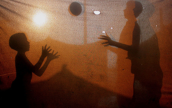 Shadow of friends playing with ball on fabric during sunset