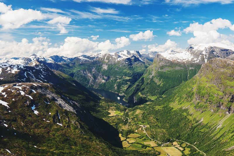 Scenic view of green mountains against cloudy blue sky at geirangerfjord