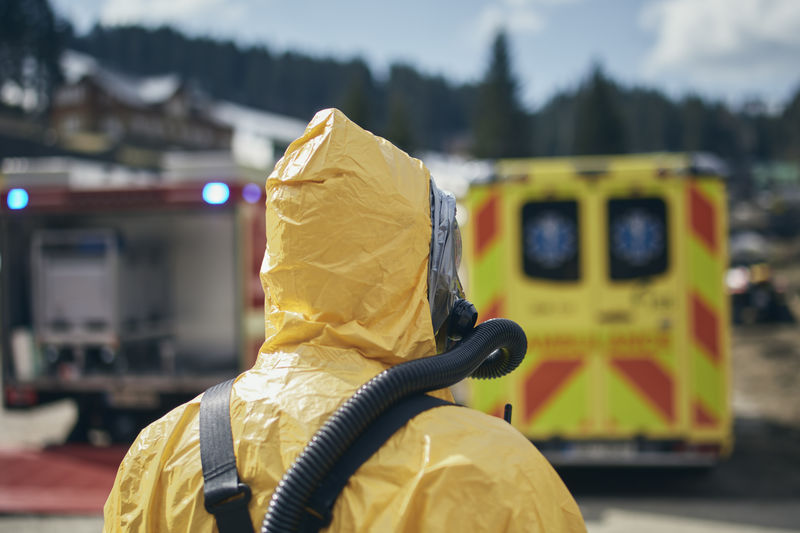 Member of biohazard team of emergency service in protective suit against ambulance and firefighters.