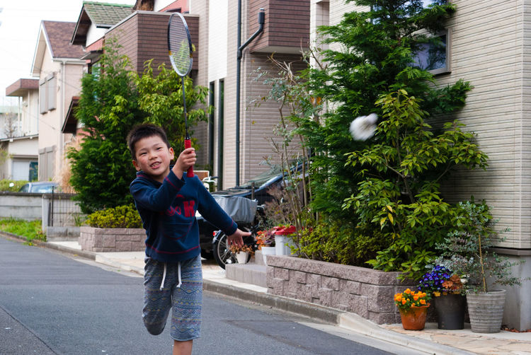 Boy playing badminton on street by house