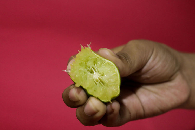 Close-up of hand holding apple against red background