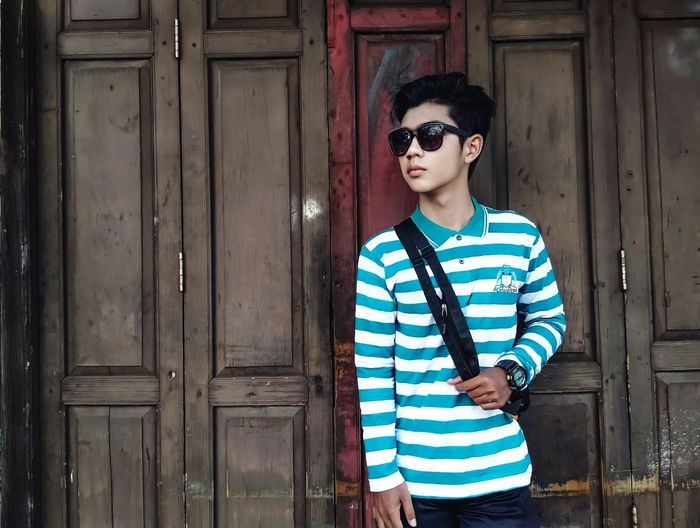 Full length of teenage boy wearing sunglasses standing against door