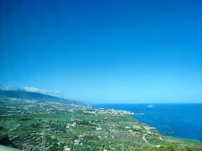 Aerial view of townscape by sea against blue sky