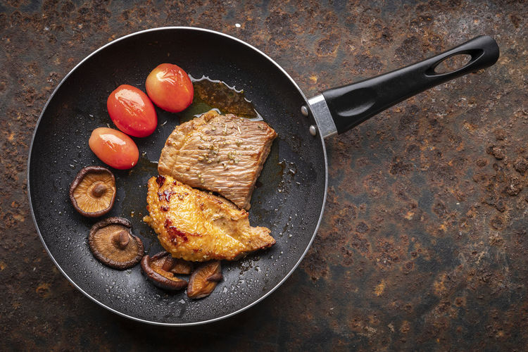 Fried beef fillet steak meat with tomato, mushroom and oregano in black pan on rusty background