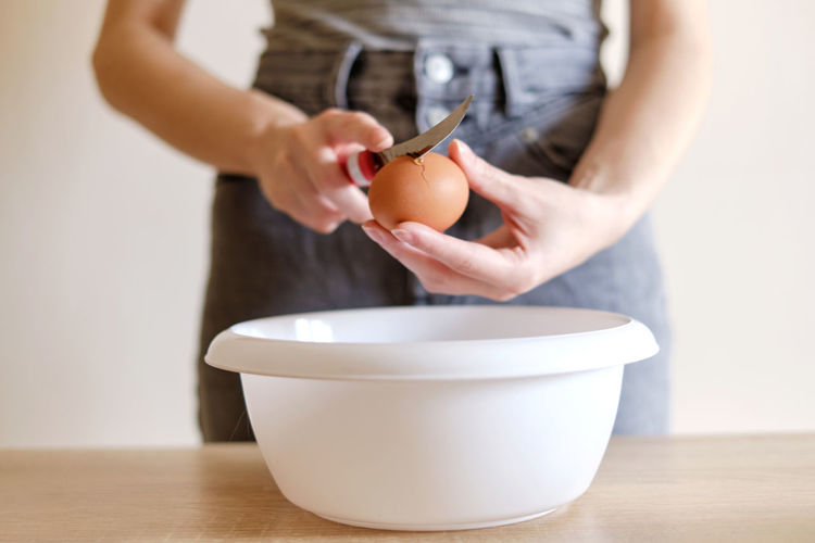 Woman breaks an egg with a knife over a plate to cook a delicious meal