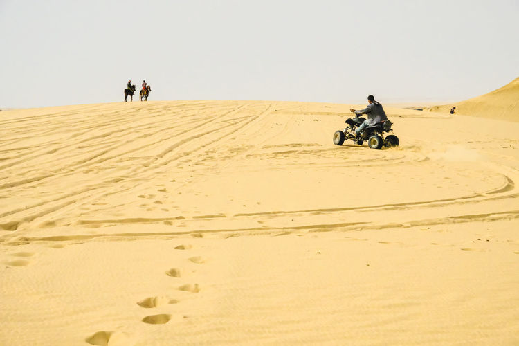 Man riding quad bike on desert against clear sky