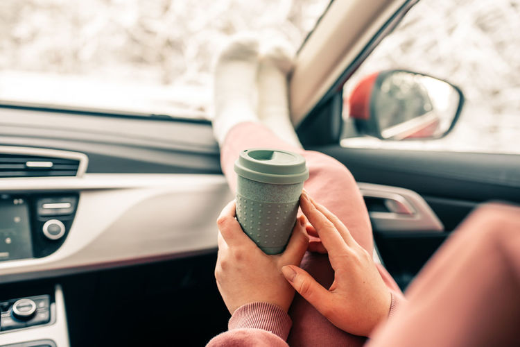 Low section of woman holding coffee cup sitting in car
