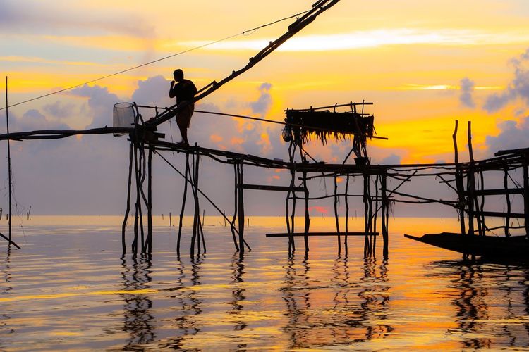 Silhouette fishing net on sea against sky during sunset