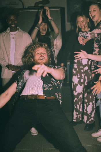 Portrait of flexible young man bending backwards dancing amidst friends at nightclub