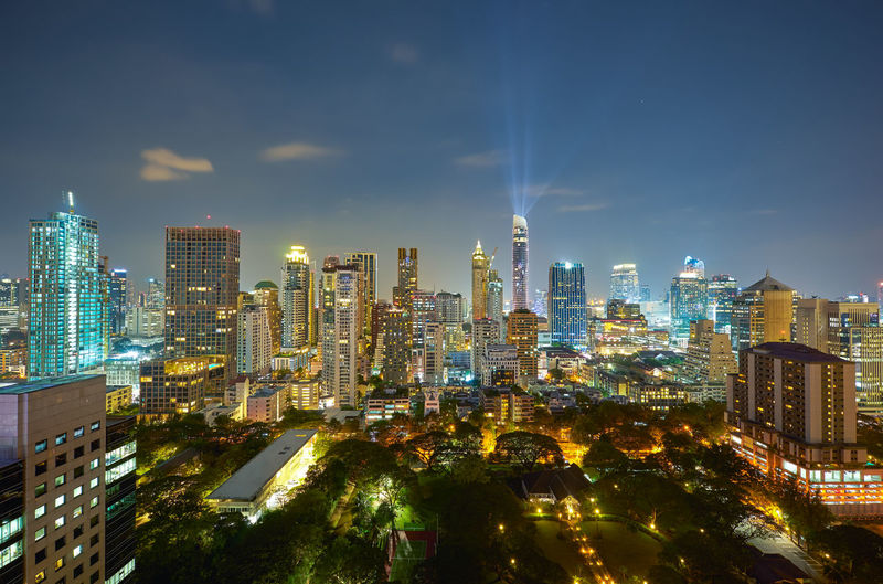 Illuminated modern buildings in city against sky at night