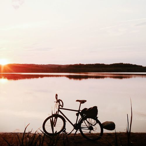 Bicycle by lake against sky during sunset