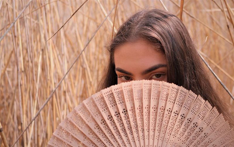 Close-up portrait of a beautiful young woman looking at camera through fan