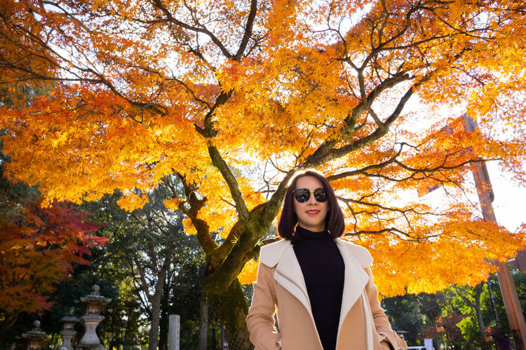 Portrait of young woman standing by trees during autumn