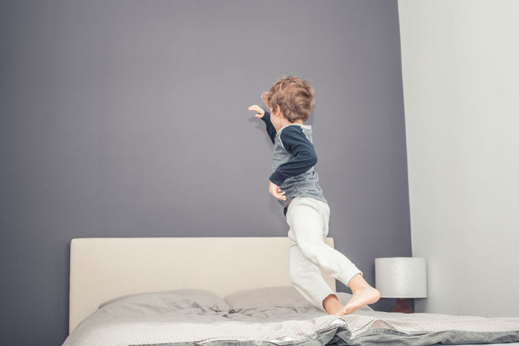 Small kid jumping on the bed and having fun in the evening.