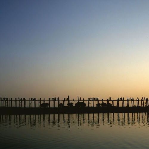 Silhouette pier in calm sea at sunset