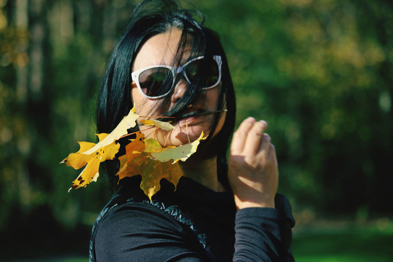Portrait of young woman wearing sunglasses holding leaf outdoors