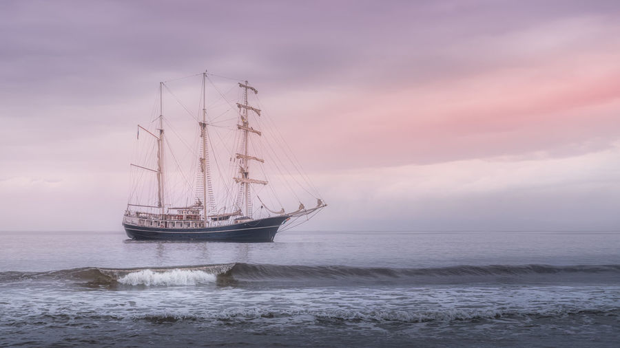 Rolling wave in front of tall ship covered in haze, anchored near northern ireland coast