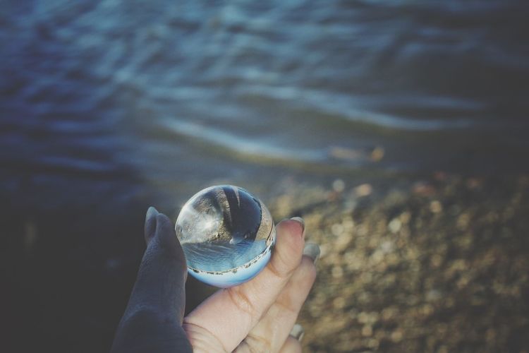 Cropped hand of woman holding crystal ball at beach