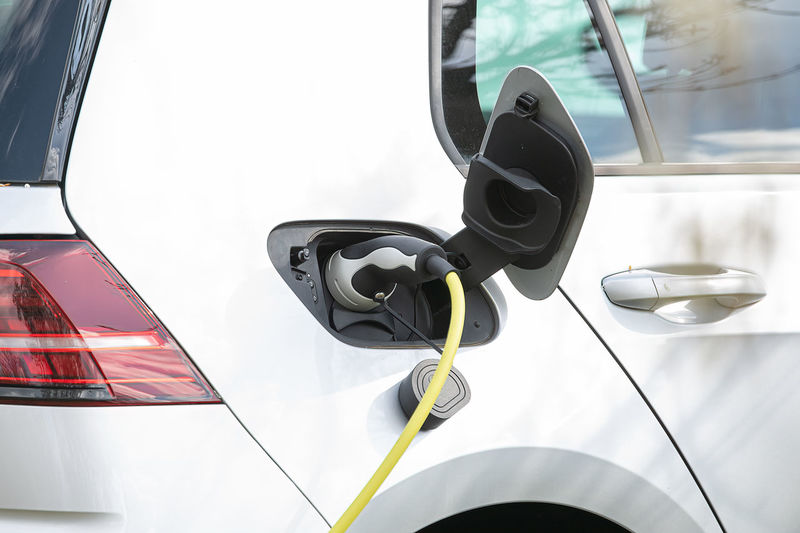 Plug in adapter in car charge battery of electric car next to a charging station with yellow cable 