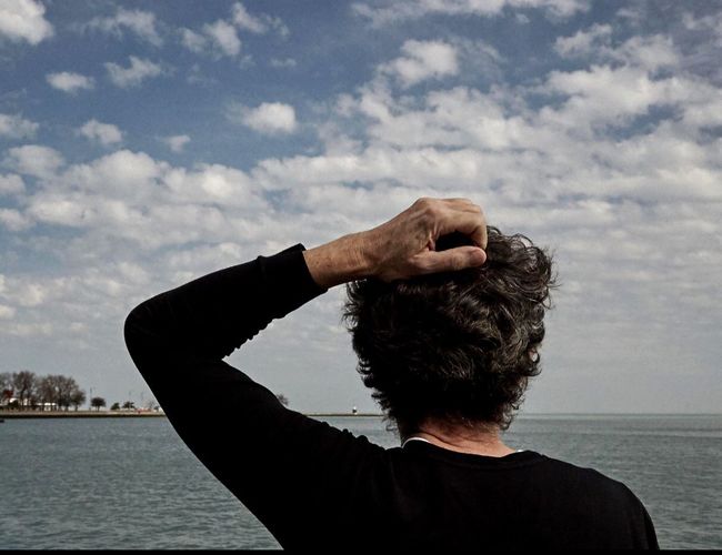 Rear view of person hand on head against river and cloudy sky