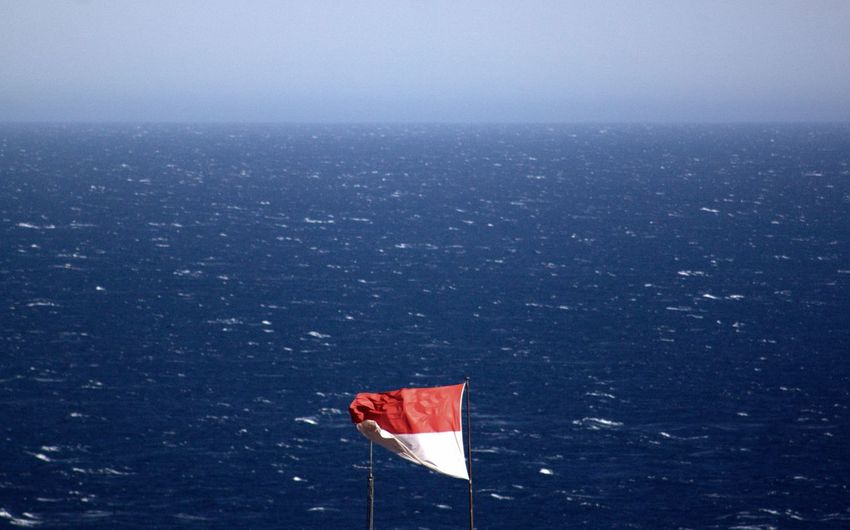 Waving flag by sea against sky