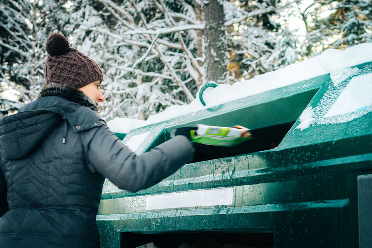Rear view of woman putting garbage in can during winter