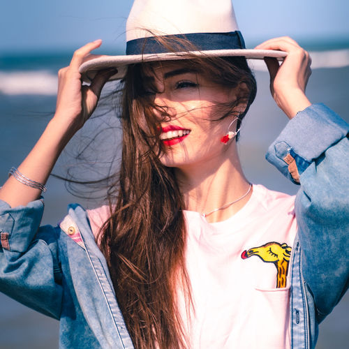 Close-up of smiling young woman wearing hat standing on beach