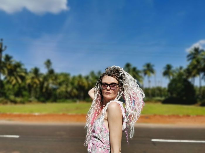 Woman wearing sunglasses standing by road against sky