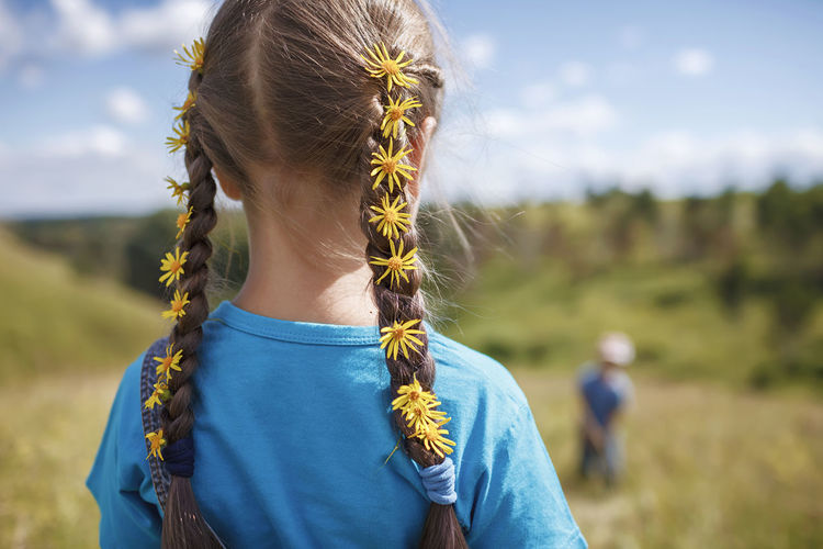 Rear view of girl wearing flowers in hair while standing on field