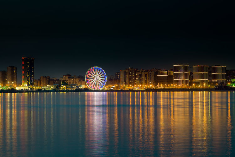 Illuminated ferris wheel in city against sky at night