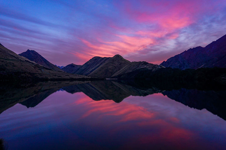 Scenic view of lake by mountains against sky at sunset