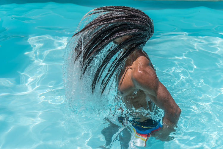 Young black man with dreadlocks inside a pool moving his wet hair in a trail of water