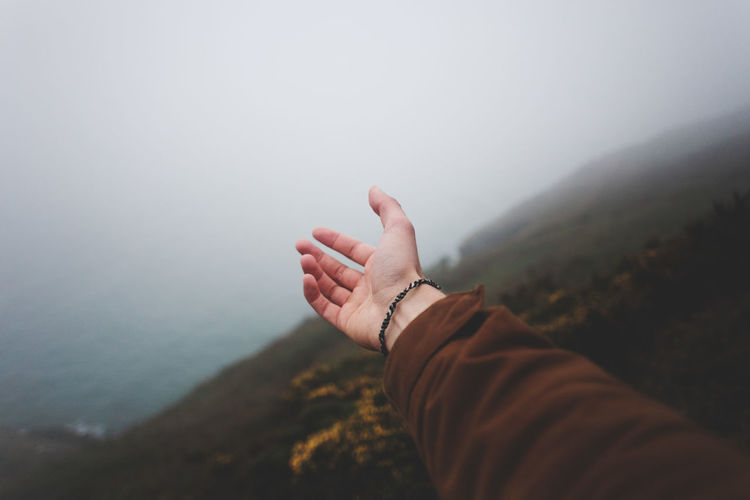Cropped hand gesturing against mountain during foggy weather