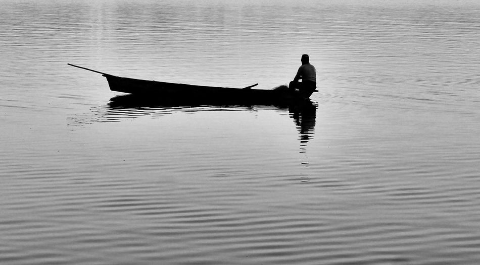 Silhouette fisherman sitting on boat in lake