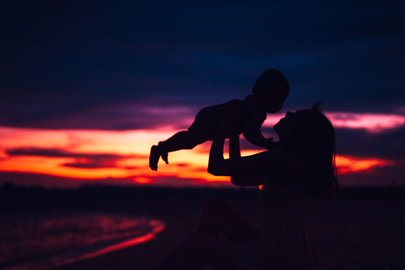 Silhouette couple kissing against orange sky