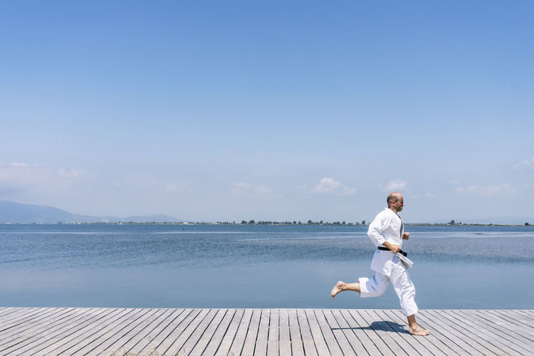 A man practices martial arts running on a wooden walkway by the sea