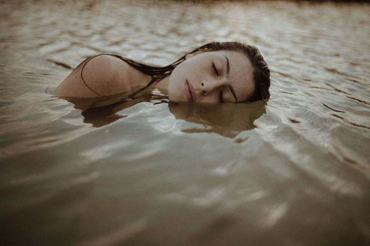 PORTRAIT OF A YOUNG WOMAN LYING ON SWIMMING POOL