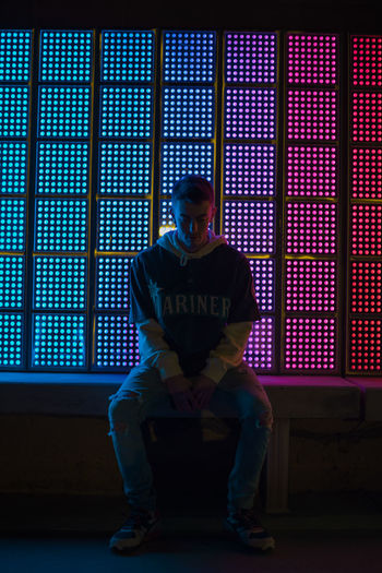Full length of young man sitting against illuminated window