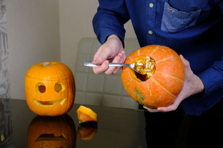 Midsection of man holding pumpkin against orange wall during halloween