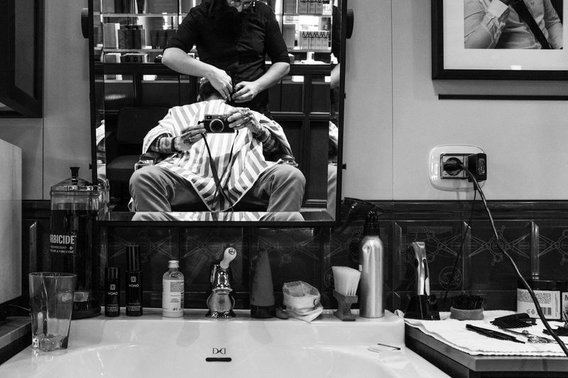 Reflection of man photographing with barber on mirror at shop