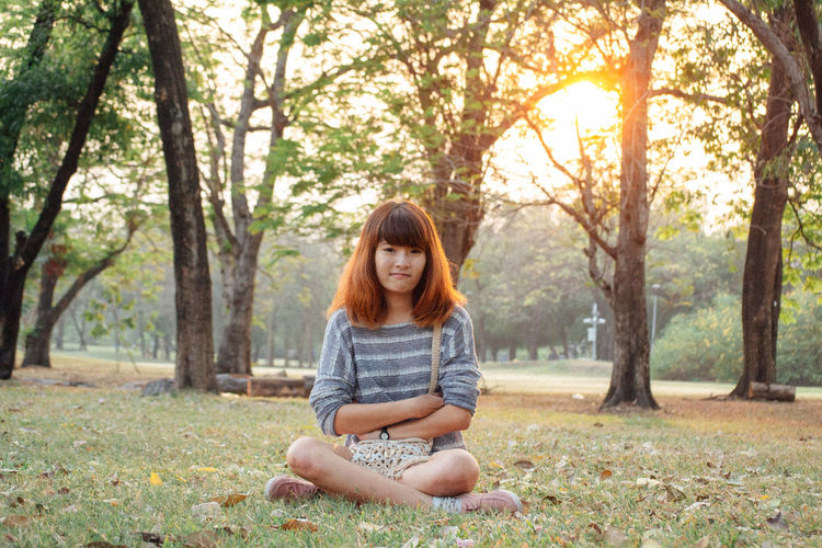 Portrait of smiling woman sitting at park during sunset