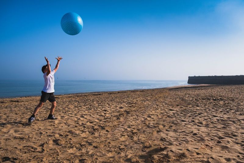Boy playing with ball at beach against sky