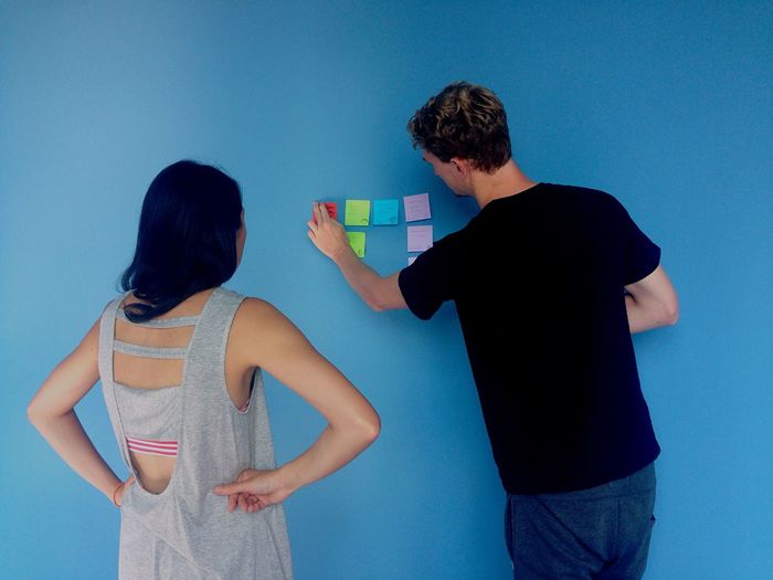 Man sticking adhesive notes on blue wall by woman