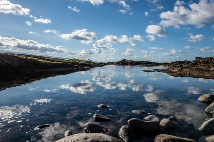 Scenic view of a natural, tidal pool with reflection of the sky with scattered clouds and rocks