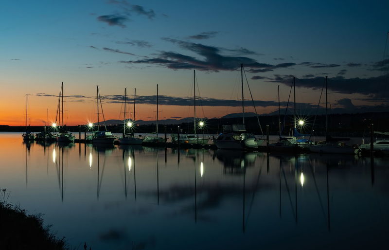 Sailboats moored at harbor against sky during sunset