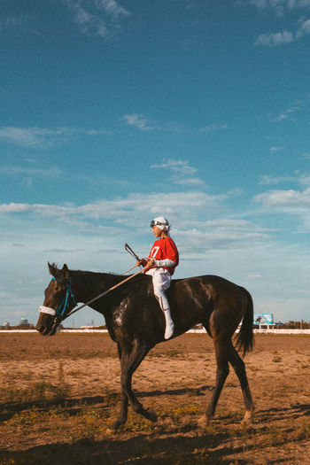 Rear view of young boy horse rider standing on field against clear sky
