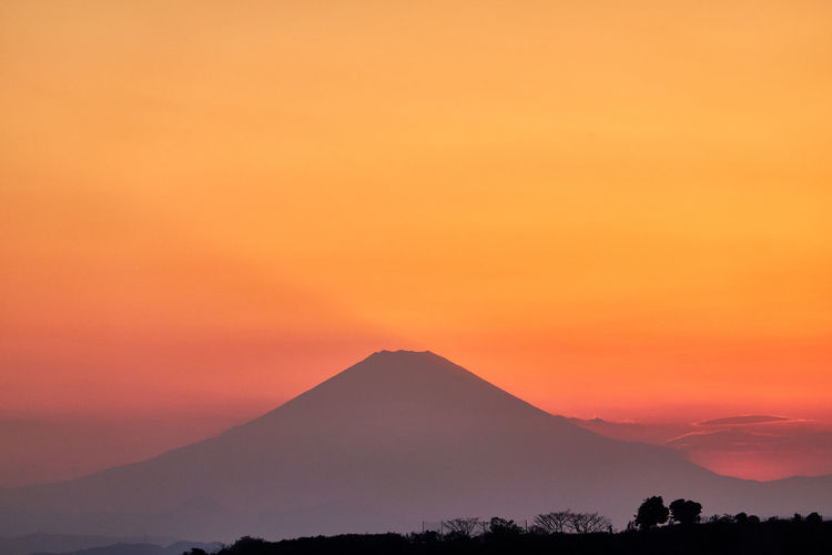 Scenic view of silhouette volcano mountain against orange sky