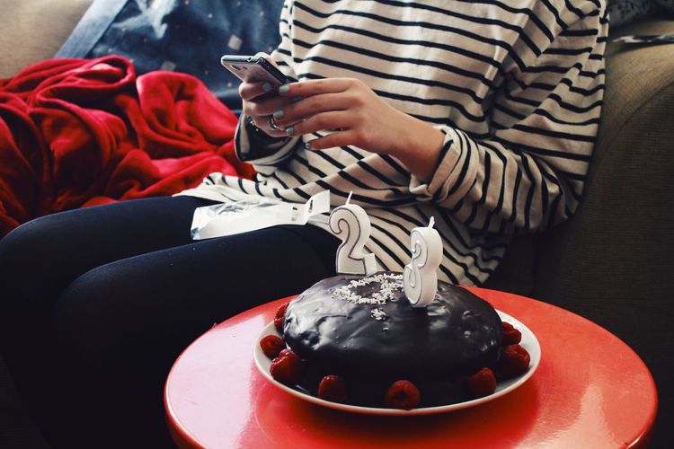 Midsection of woman using mobile while sitting by cake at home