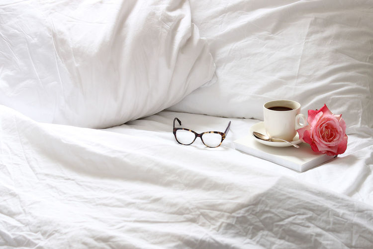 High angle view of coffee cup with rose by eyeglasses on bed