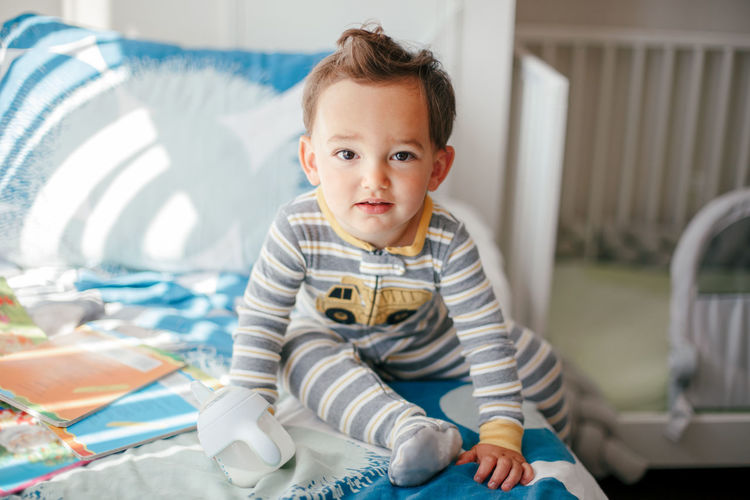 Cute adorable caucasian kid boy sitting on a bed drinking milk from kids bottle. healthy eating 